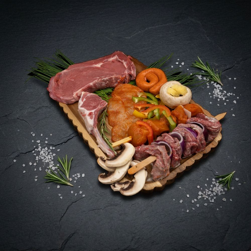 Inhoud BBQ Bulk Box: entrecote, lamskotelet, runds merguez, kiplapje, gevulde champignon, kip saté met groenten en runds shashlik op houten plank