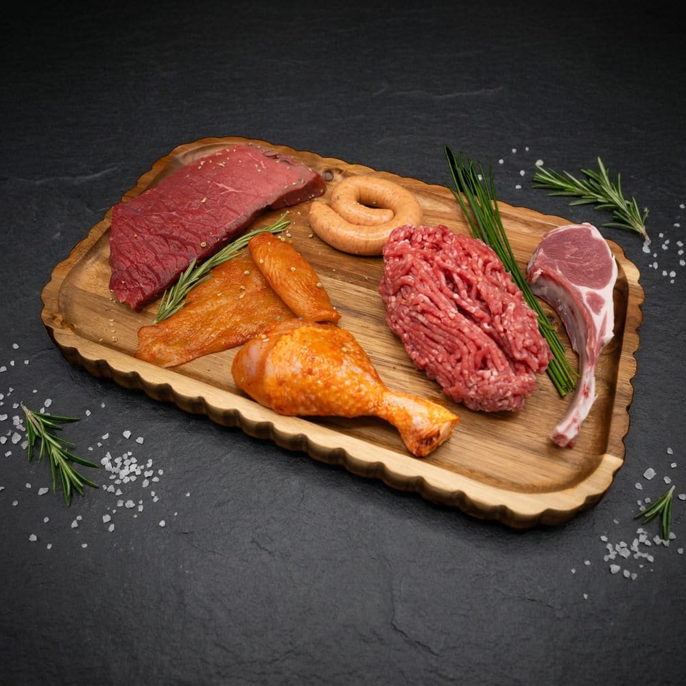 Inhoud Weekvoorraad & Vriezerbox: biefstuk, kipfilet, chipolata, rundergehakt, lamskotelet en drumstick op houten plank